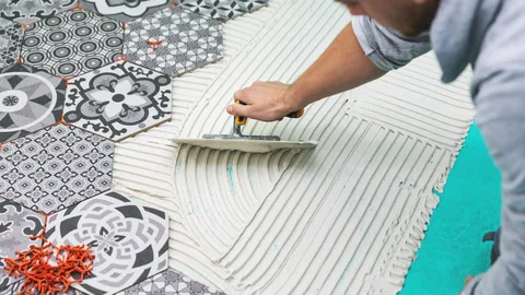 Close-up of a worker spreading striped mortar next to complex patterned black, white, and gray hexagon tiles during a custom tile installation Barrie project by YAM Home Renovation.