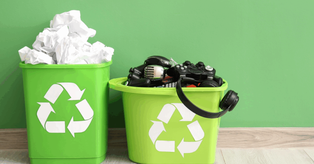 Green recycling bins filled with paper waste and electronic items such as controllers and headphones, illustrating proper disposal for E waste removal services Kent WA.